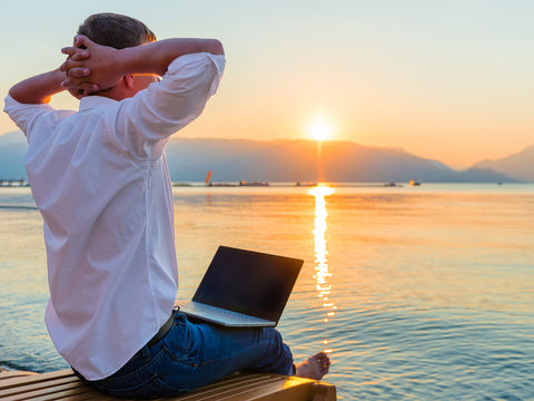 Man overlooking beach sea sunset with laptop in his lap