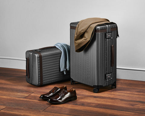 Two hard-shell grey suitcases with clothes draped over them