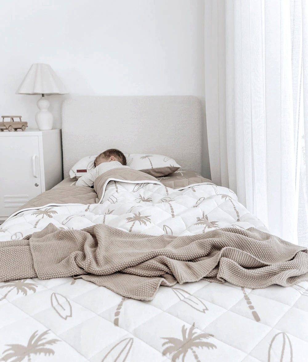 Cozy children's bedroom with a child asleep in palm-printed bedding, soft knits, and calming neutral tones