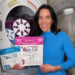 Wad-Free for Bed Sheets and Wad-Free for Blankets & Duvet Covers blue and pink packages held by woman in blue dress next to an open clothes dryer showing the white products