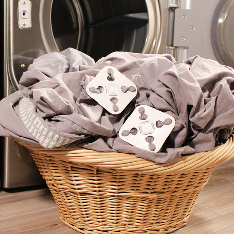 A wicker basket holding grey sheets with White Wad-Frees attached sitting on the floor with a washer and dryer in the background