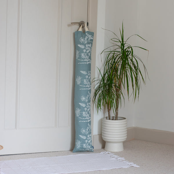 Duck Egg Blue Draught Excluder from the Garden Design by Helen Round leaning against a door next to a Dragon Tree houseplant