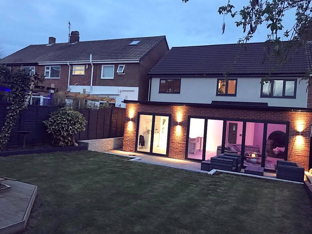 Night time view of a Scandinavian inspired white modern contemporary open plan kitchen living room with bi folding doors.