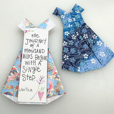two blue origami dresses, one with a quote on it reading "the journey of a thousand miles begins with a single step." Lao Tzu