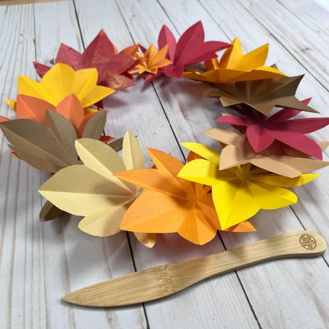 fall colored paper leaf wreath shot with a bamboo folding tool next to it