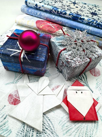 origami angel and santa clause in front of two presents wrapped in blue and silver gel printed washi paper and a stack of gel printed washi paper in the background
