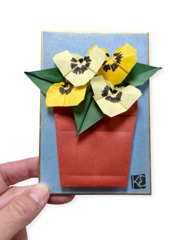 hand holding a shikishi board decorated with origami pansies coming out of an origami pot