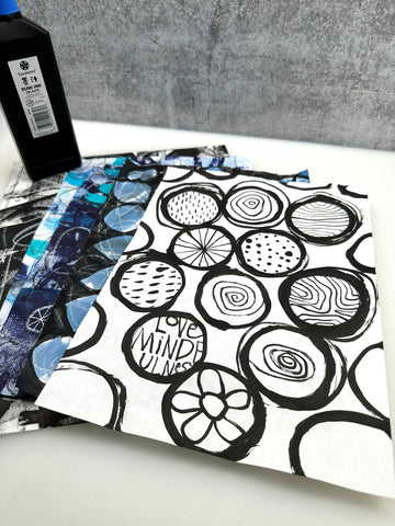 spread of papers with abstract black ink circles with designs and a bottle of ink in the background