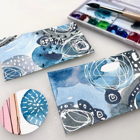 picture of abstract watercolor doodles on two artist trading cards and a cut out circle with a paint filled palette and paint brush in the background