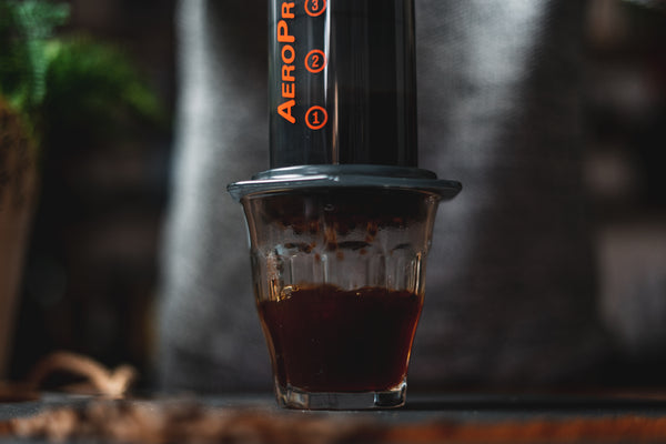 A glass filling with coffee, an AeroPress sitting on top.