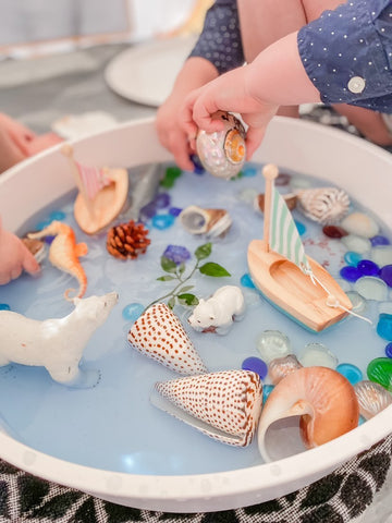 Bowl of light blue jelly full of shells, animal toys and wooden boats