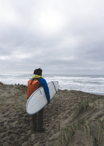 Adam looks out over the ocean holding a surfboard in Newport, Oregon.