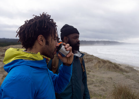 Adam and Kenny looking out at the break at South Jetty, Newport Oregon. Adam drinks out of the cup lid of a Stanley vacuum bottle.