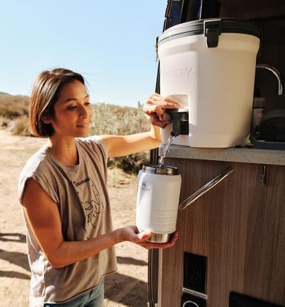 Woman camping with her family, filling Stanley's IceFlow™ Flip Straw Jug from The Fast Flow Water Jug.