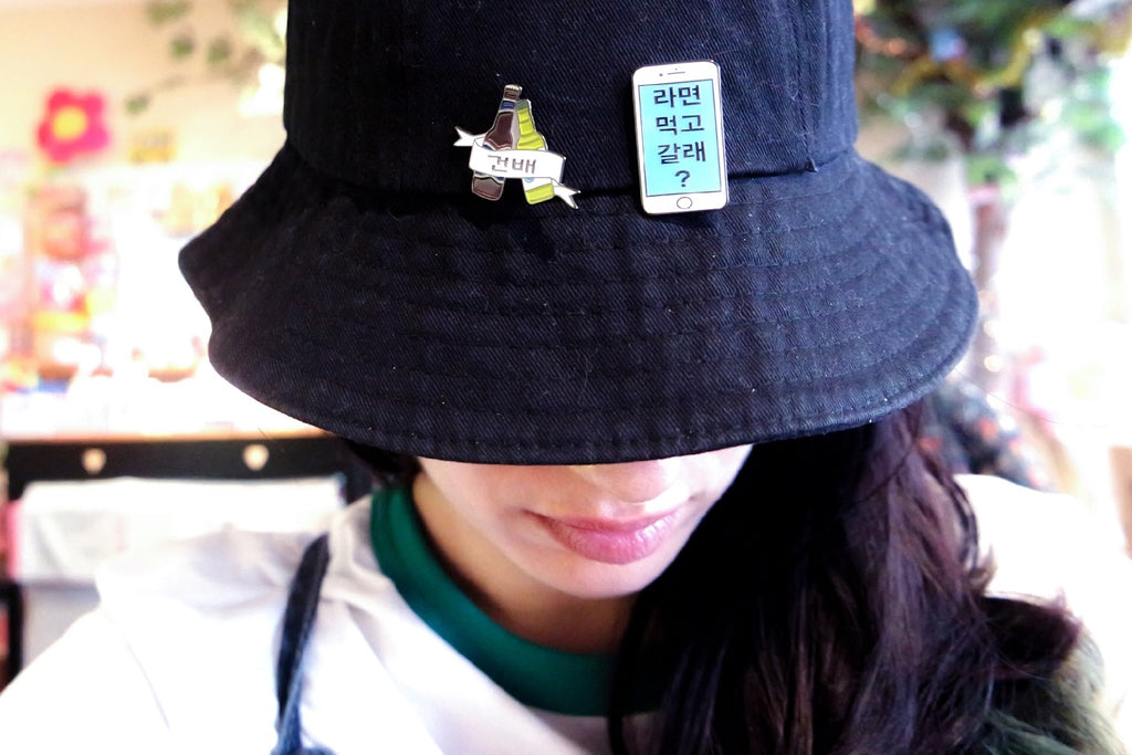 Woman looking down to show off black bucket hat with two enamel pins.