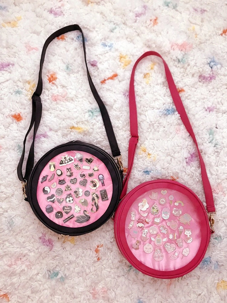 A black and pink Ita bag with enamel pins inside of them.