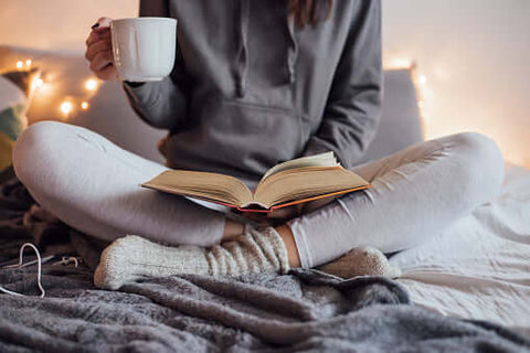 Woman in bed with tea reading a book