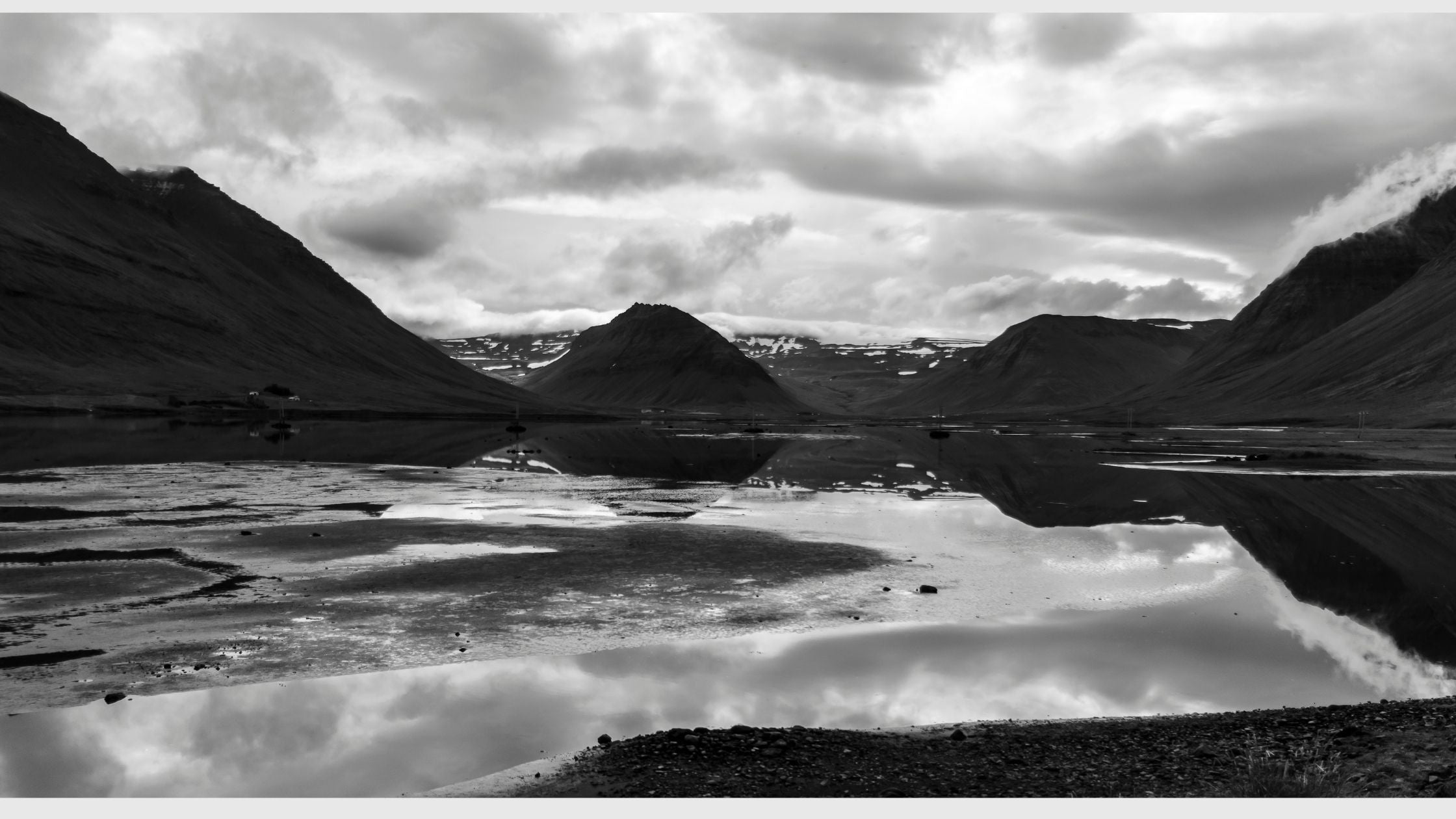 A black and white panoramic view of mountains and a lake in front. 