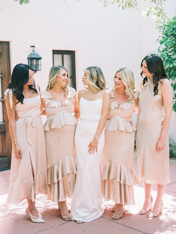 Bridal party in champagne colored dresses stand by the bride in classic white gown.