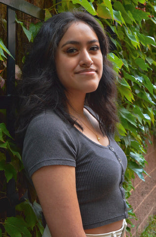 A professional photo of a young woman standing against a wall covered in ivy