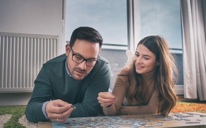 young couple doing puzzle floor window background