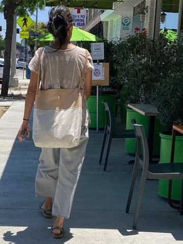 Woman walking outside wears a combination of natural denim & natural-veg tan leather bag on her back (like a backpack). This bag is artisan made and handcrafted.