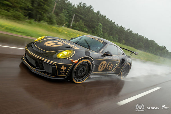 A black and gold Porche drives on a highway in wet conditions