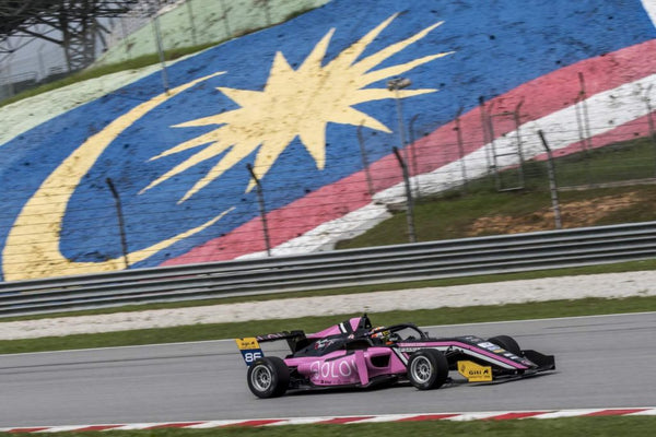 The Pink Oloi F3 car races on the track with the Malaysian flag painted in the grass in the background