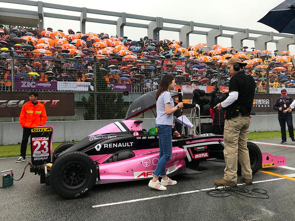 Asian Formula Renault media team members conduct an interview near the pink Oloi car on the starting grid