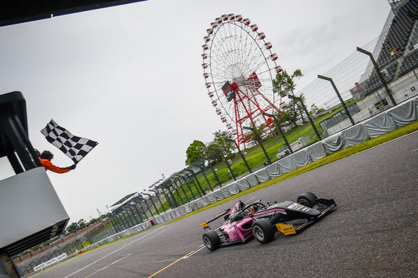 The checkered flag waves above the pink Oloi F3 car as it crosses the finish line