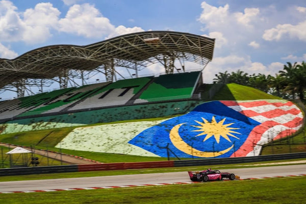 The pink Oloi F3 car races past a Malaysian flag painted in the grass bordering Sepang Circuit