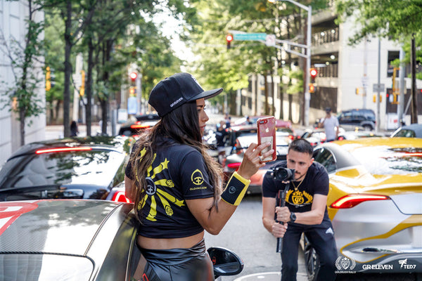 A man photographing a woman wearing an Oloi/goldRush Rally shirt among cars