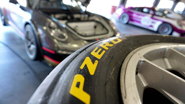 Stack of racing tires with Oloi's Porsche 911 Cup car in the background