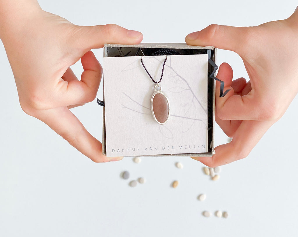 pocket treasure silver necklace with stone held by 2 hands daphne van der meulen jewelry
