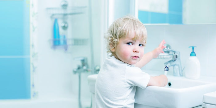 un petit garçon ouvre le robinet dans une salle de bains avec des carreaux bleus