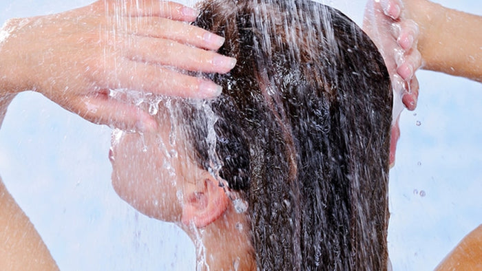 Frau von hinten gesehen, die das Shampoo im Haar mit Wasser spült