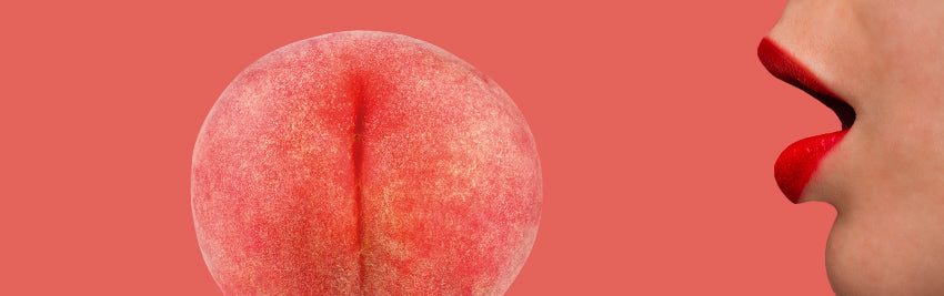 A close up of a peach that looks like a butt with a person mouth standing close to it