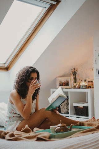 woman reading book and drinking tea by window