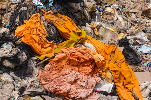 orange clothing lays on top of a pile of trash at a landfill