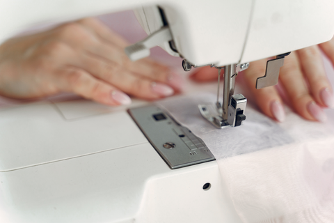 woman's hands feeding fabric through sewing machine
