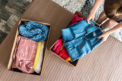 Woman participating in a clothing swap. She is placing a chambray shirt into a box while another box of clothing sits opposite her