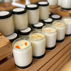 A row of candles in clear tumblers sits on a crate. Each has decorative botanical elements as a topper.