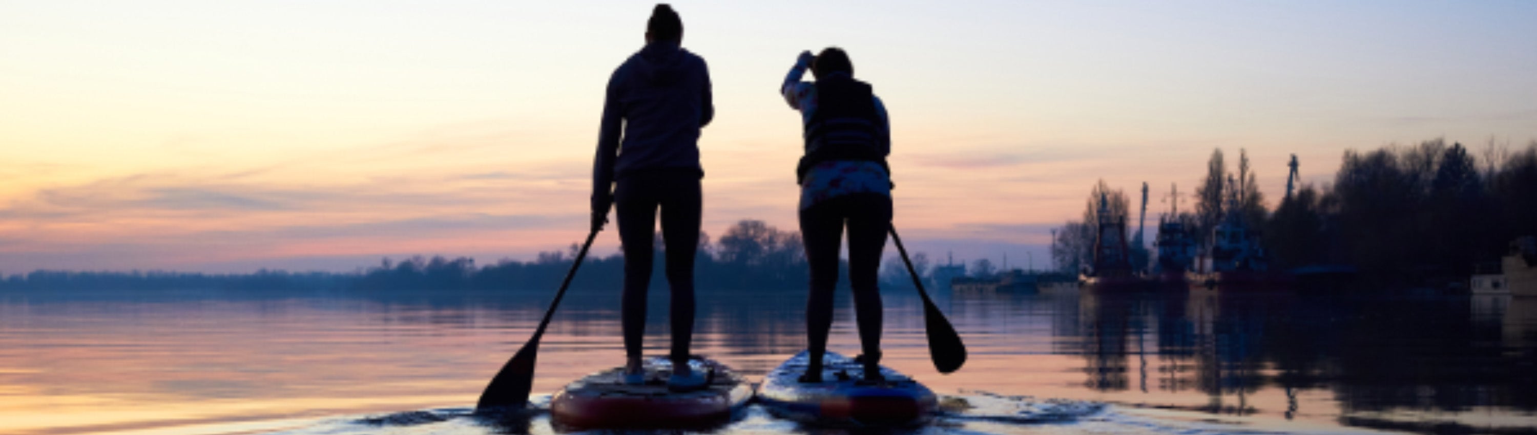 two women are wrapped up warm, paddle boarding on a crisp winter morning