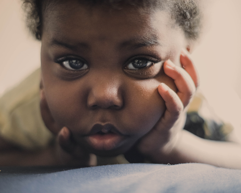 baby with blue eyes looking into camera and holding their face