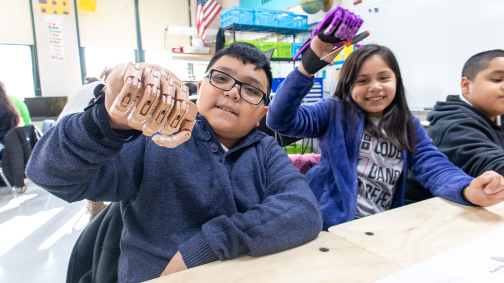 3rd graders at Peck Elementary show a completed 3D printed hand they assembled during a workshop in their classroom with e-NABLE