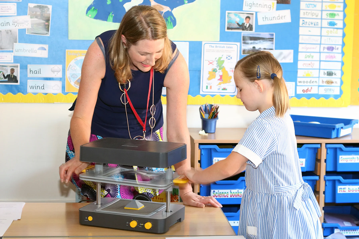 A teacher shows a young student how to use a Mayku FormBox vacuum former in the classroom