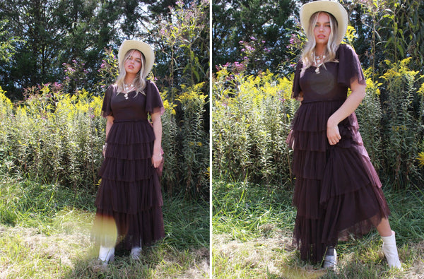 Jes is wearing a purple tulle dress, hat, and white boots in a field of flowers