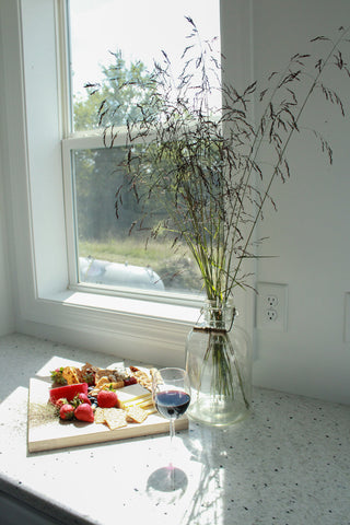 cheese and fruit plate on a white countertop with wild flowers.