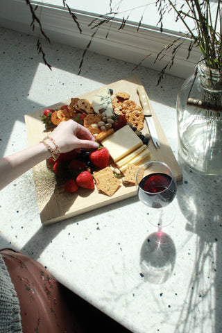 gal reaching over a plate of yummy cheese and fruit with a glass of wine sitting on the counter