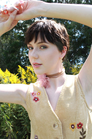 our model Kennedy is wearing the trinity vest and a leather flower necklace. she has a pixi hair cut and is standing in a field of goldenrod flowers